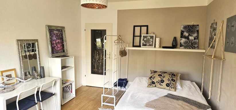 Helles Schlafzimmer mit Bett, Schreibtisch und dekorativen Bildern an der Wand.